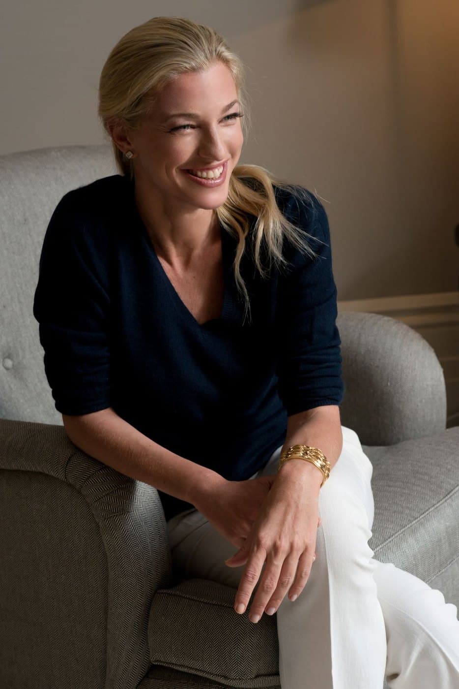 Nicole Junkerman seated in an armchair in a navy jumper, smiling in soft indoor light